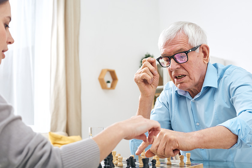 senior disable man eyeglasses shirt playing chess female social worker