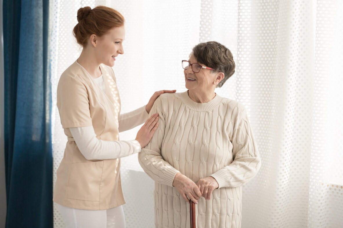 Professional,Caregiver,In,Uniform,Talking,To,And,Assisting,An,Elderly